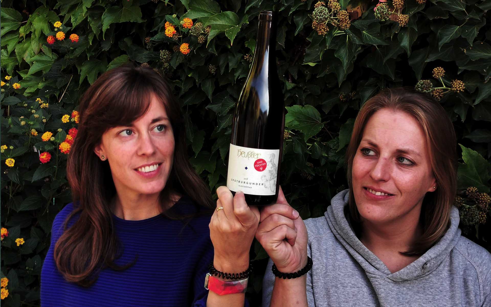 Nina und Meike halten zusammen eine Flasche Spätburgunder "& Töchter" hoch.