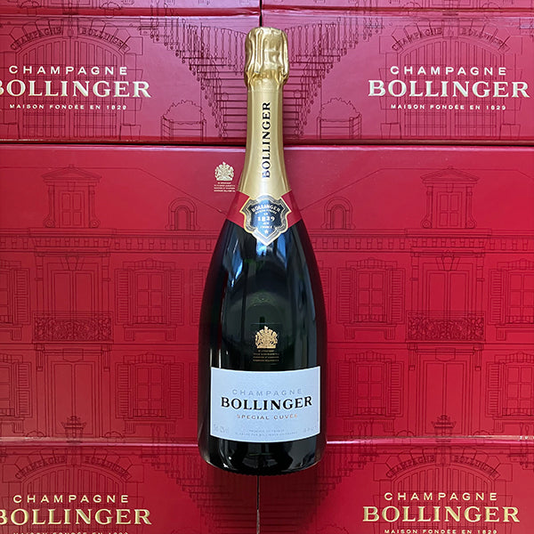 A bottle of Bollinger Champagne Special Cuvée on a red background of Bollinger boxes. The royal warrant is visible on both the bottle and the box.